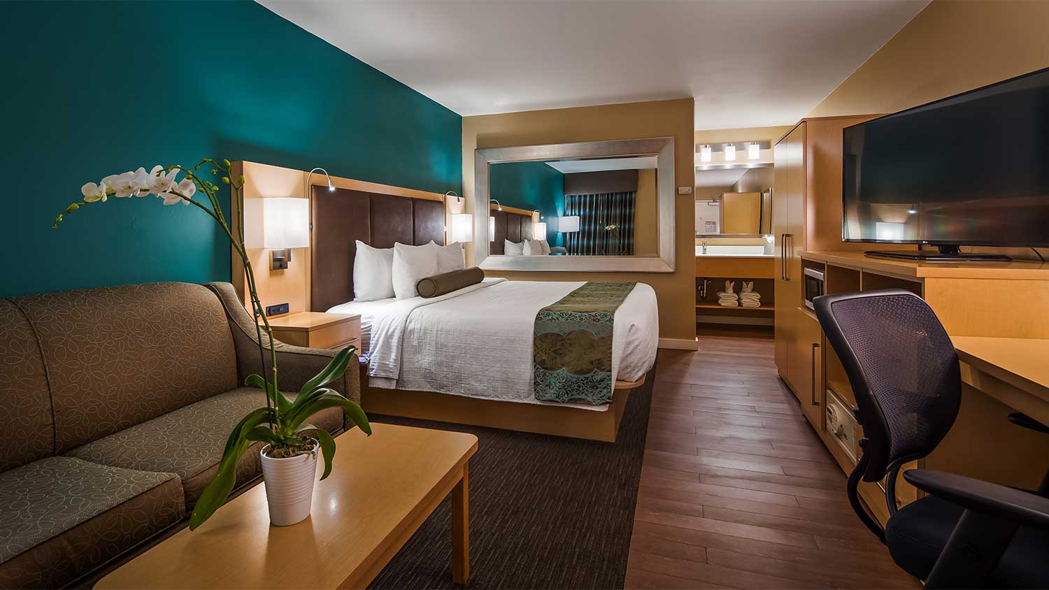 View of single king bed room displaying sofa sitting area, flatsreen tv, office chair and bathroom entrance